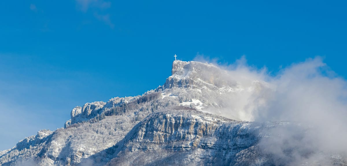 Croix blanche du Nivolet dominant le massif des Bauges, perchée sur un sommet rocheux face aux Alpes enneigées